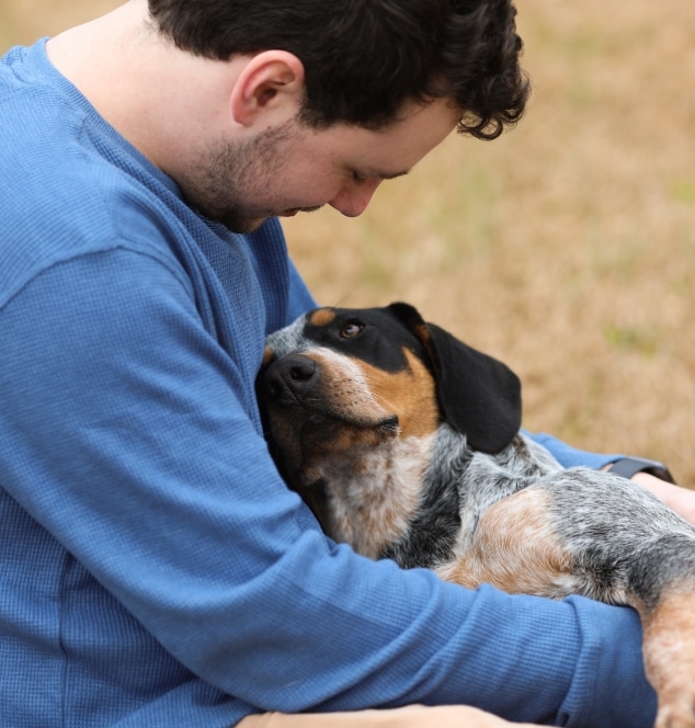 Dog owner sitting on grass with dog in their lap looking up at owner